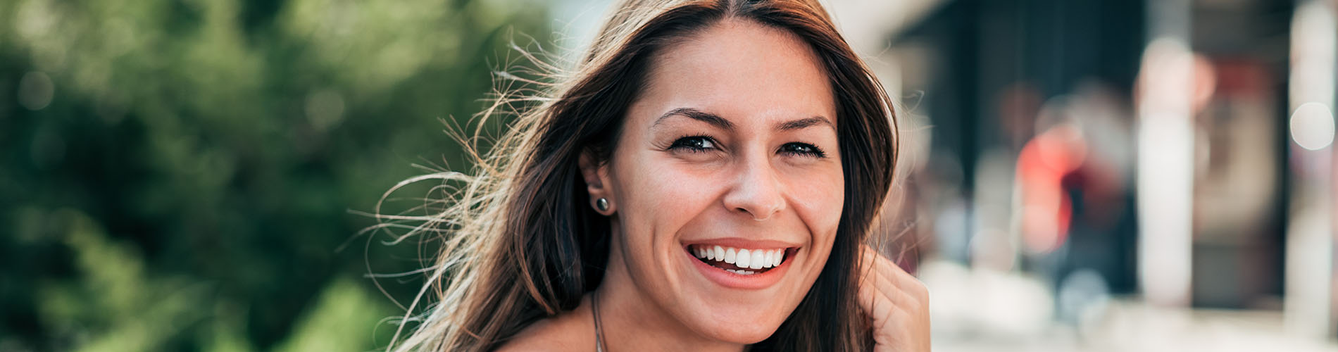 The image is a photograph of a woman with light skin, smiling at the camera. She appears to be in her late twenties or early thirties and has long hair. Her eyes are looking directly at the camera, and she is holding up her index finger near her mouth as if she s making a point or emphasizing something. The background is plain and light-colored, which suggests that this could be a stock photo used for various purposes such as advertising, personal branding, or lifestyle content.
