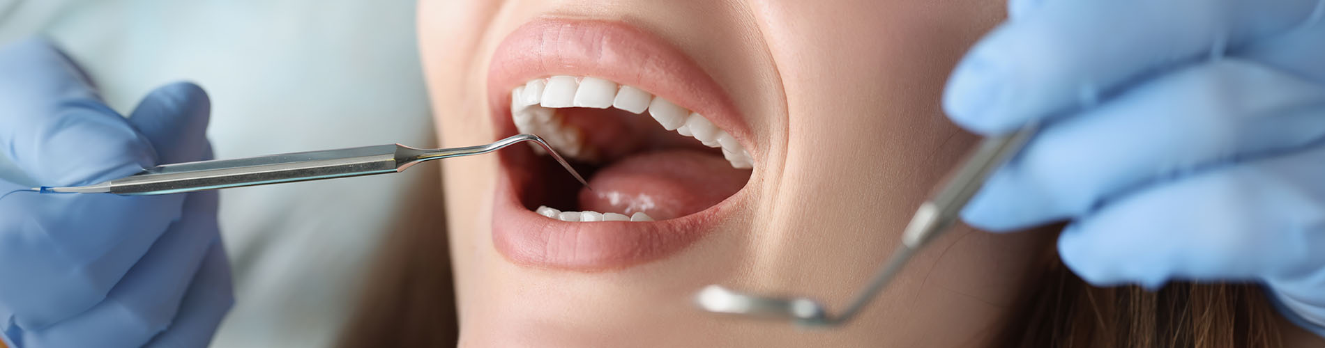 A person is seated in a dental chair, receiving care from a dental professional who stands behind them.